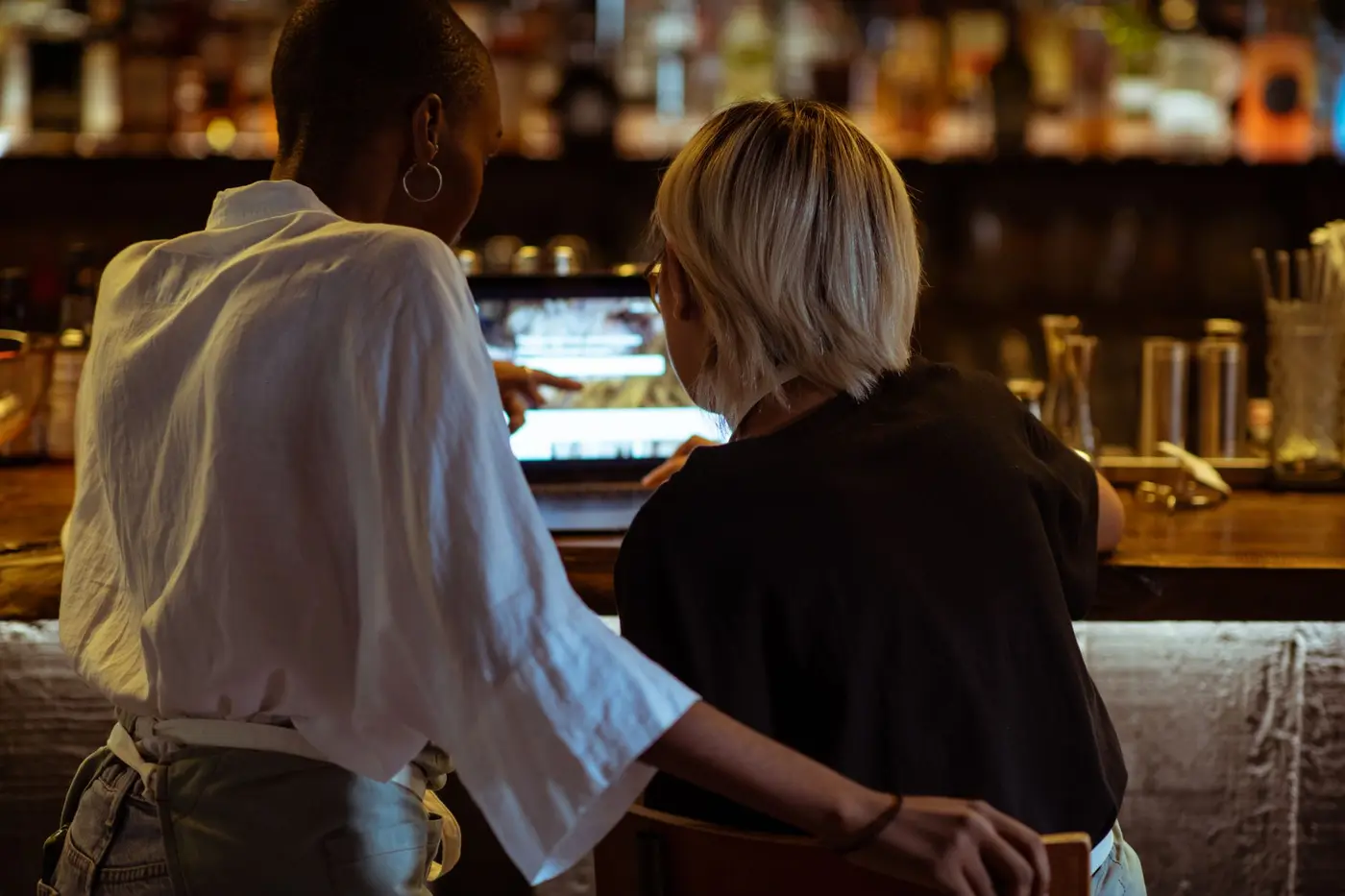 Two restaurant staff at the bar counter looking at a web page on a laptop